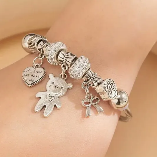 PULSEIRA EM AÇO INOXIDÁVEL, ELÁSTICA, COM PINGENTES DE CORAÇÃO, URSO E LAÇO, BANHADA A PRATA 925